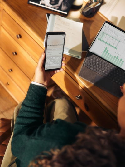 Person holding phone near laptop and tablet on desk